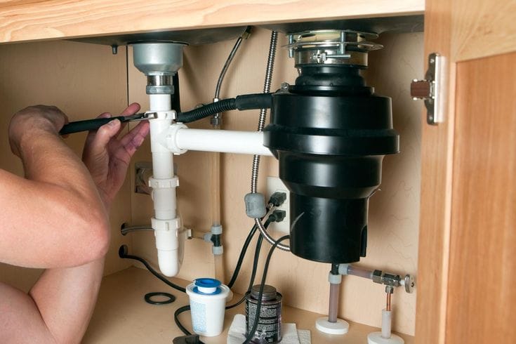 Plumber installing a garbage disposal beneath a kitchen sink in Lutz